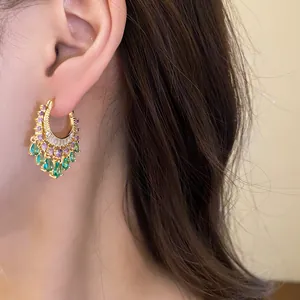 Close-up of elegant gold hoop earrings with purple and green zircon teardrops