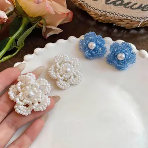 Primer plano de una mano sosteniendo un elegante pendiente de flor con cuentas.