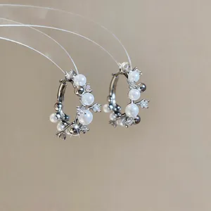 Close-up of elegant silver hoop earrings with white pearls and sparkling zircons.
