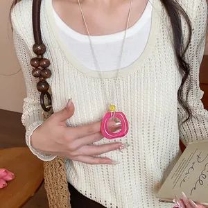 Primo piano di una collana con pendente geometrico in acrilico rosa su un maglione