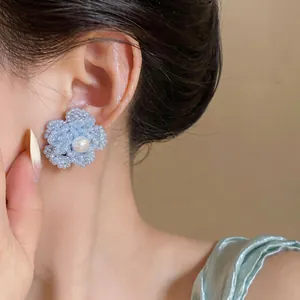 Primer plano de un pendiente de flor con cuentas azul claro y perla blanca central