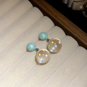 Detailed macro view of resin stud earrings with colorful polka dots inside clear spheres.