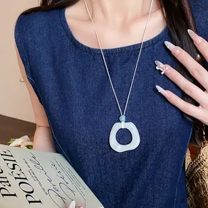Dettaglio di una collana con ciondolo geometrico in acrilico marmorizzato su denim