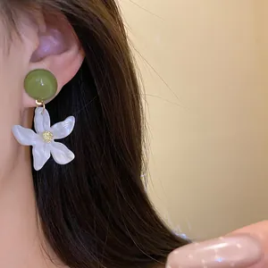 Detailed close-up of a white resin flower earring with a green round stud on ear