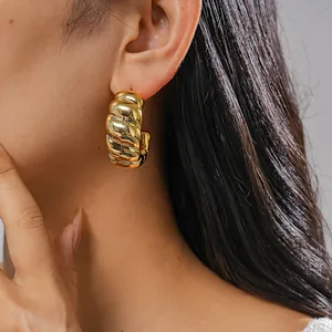 Nahaufnahme eines klobigen goldenen Creolen-Ohrrings mit polierter Oberfläche am Ohr
