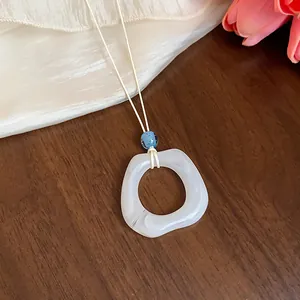 Primo piano di un ciondolo ad anello in acrilico marmorizzato bianco su cordino crema.
