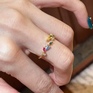 Nahaufnahme eines farbenfrohen Weizenähren-Goldrings mit lebendigen Steinen am Finger