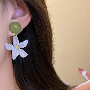 Detailed view of elegant white floral pendant earrings with green resin top on ear