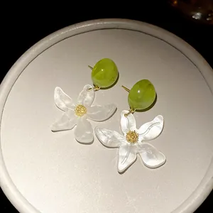 Detailed close-up of white resin flower earrings with green beads and pearlescent texture