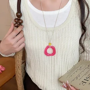 Primo piano di una collana con pendente geometrico in acrilico rosa su maglia