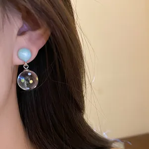 Macro detail of minimalist resin drop earrings with blue polka dot pendant worn on ear.