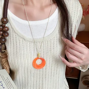 Dettaglio di una collana con ciondolo in acrilico arancione su un maglione di maglia