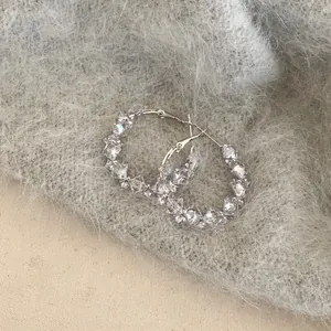 Detailed macro view of sparkling geometric zircon hoop earrings on soft grey texture