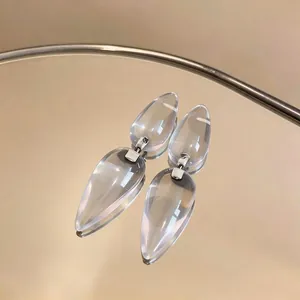 Elegant clear resin teardrop earrings with silver needle on a reflective golden tray