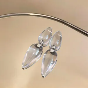 Elegant clear resin teardrop earrings with silver pins reflecting on a mirror surface.
