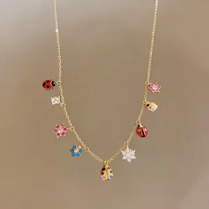 Detailed macro shot of a gold necklace featuring enamel ladybugs and zircon flowers.