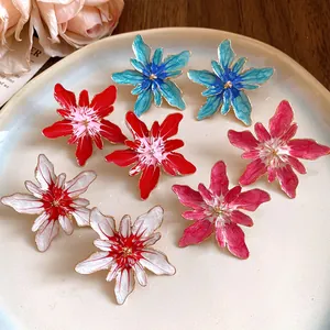 Close-up of vibrant colorful enamel flower stud earrings displayed on a beige ceramic plate.