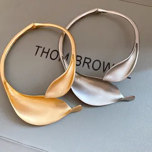 Detail shot of matte gold and silver leaf-shaped collar necklaces on a grey surface.