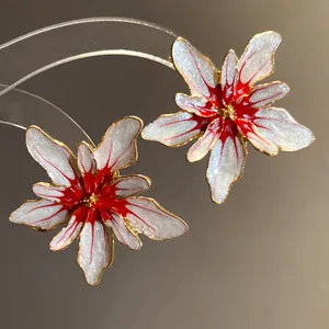 Close-up of elegant white and red enamel flower stud earrings with shimmering gold edges