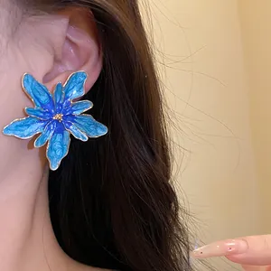 Detailed macro view of a large blue enamel flower stud earring worn on the ear with gold edges