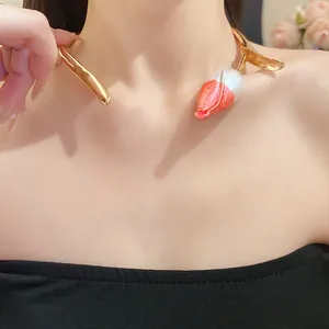 Detailopname van een goudkleurige tulp-halsketting met oranje en witte lakaccenten.