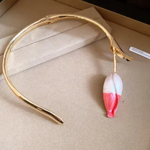 Detailopname van een goudkleurige choker met een roze en wit geschilderd tulpknopje als detail.