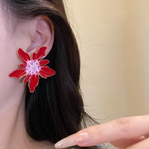 Detailed close-up showing a red enamel flower stud earring with gold edges on a model's ear