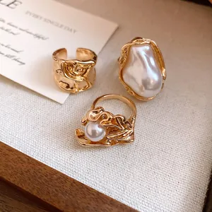Gros plan de bagues plaquées or avec perles baroques irrégulières et bandes métalliques texturées