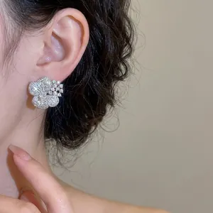 Sparkling silver flower stud earrings with pavé zircon stones on an ear model