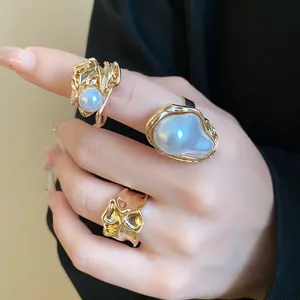 Gros plan de bagues en perles baroques et d'un anneau en or texturé sur la main