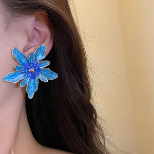Detailed view of large blue enamel flower stud earrings with golden edges worn on a model's ear