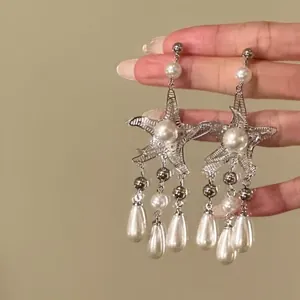 Close-up of elegant silver-colored starfish earrings with long pearl tassel drops