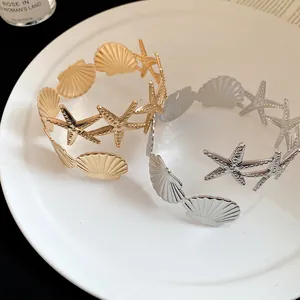 Detailed view of gold and silver starfish and seashell cuff bracelets on a white plate