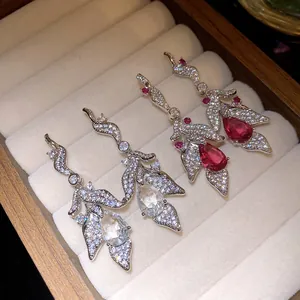 Detailed macro view of silver zircon leaf drop earrings with red and clear crystal pendants