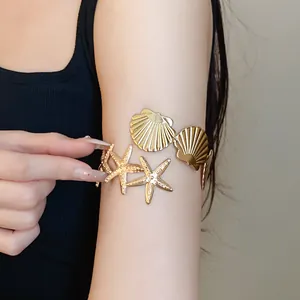 Detailed view of a golden metal starfish and seashell armlet on a model's arm.