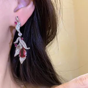 Detail shot of silver needle leaf drop earrings featuring red pear-shaped zircon stones