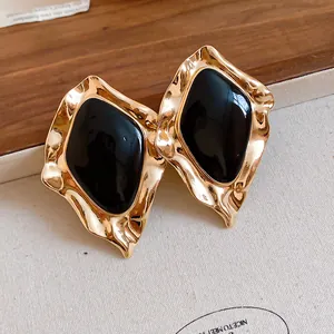 Detail view of vintage irregular gold earrings with black enamel drop oil center