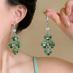 Detail view of green zircon flower tassel earrings worn on ear and held by hand