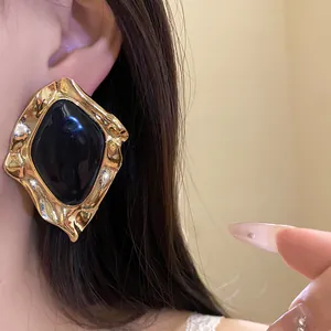 Close-up of vintage geometric black enamel stud earring with an irregular gold-tone textured frame