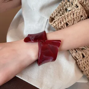 Detalle de un brazalete de resina geométrico irregular rojo oscuro en la muñeca de una modelo