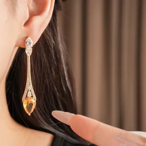 Primo piano di orecchini pendenti placcati oro 18k con zirconi gialli e trasparenti.