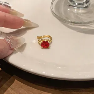 Dettaglio di un earcuff placcato oro 18 carati con uno zircone rotondo rosso brillante.