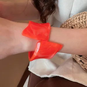 Vista detallada de un brazalete de resina naranja con forma geométrica irregular en la muñeca.