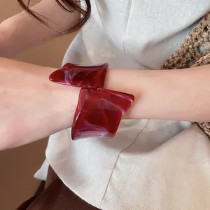 Primer plano del brazalete geométrico de resina roja oscura usado en la muñeca de una mujer