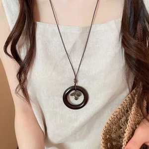 Detail view of a retro circular leaf pendant necklace worn by a model in linen top