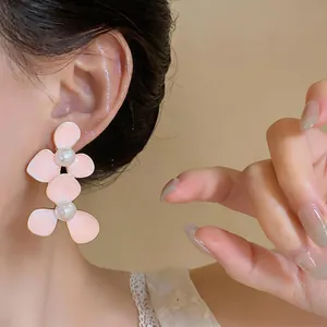 Elegante roze emaille bloemenoorbellen met parels op het oor van een Aziatisch model