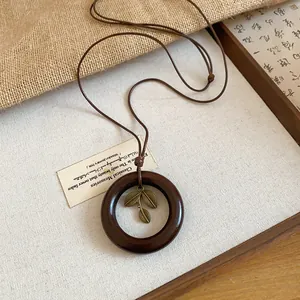 Close-up detail of vintage wooden circle necklace with an antique bronze leaf pendant.