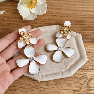 Primer plano de elegantes pendientes de flores de esmalte blanco con centros de cristal