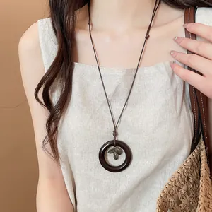 Close-up of vintage ethnic style long necklace with dark wood circle and metal leaf pendant.