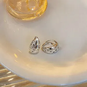 Gros plan sur des créoles géométriques en argent serties de zircons sur une assiette